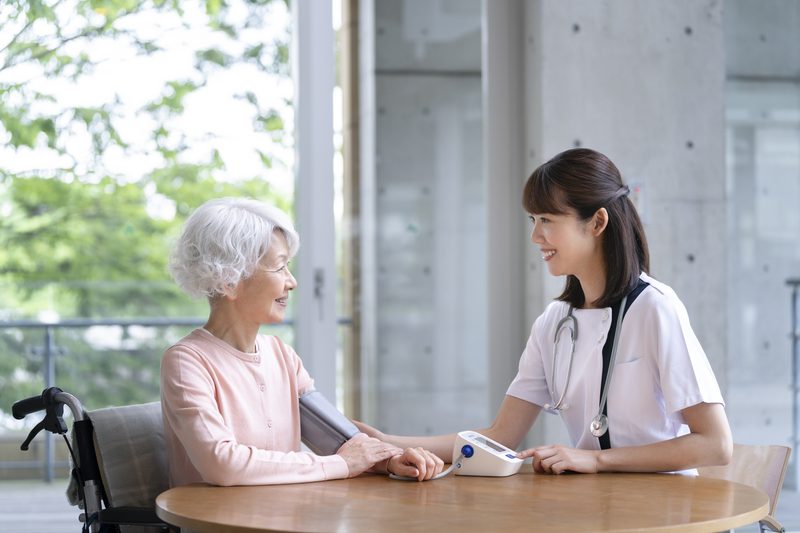 施設のテーブルで高齢女性と話をする看護師