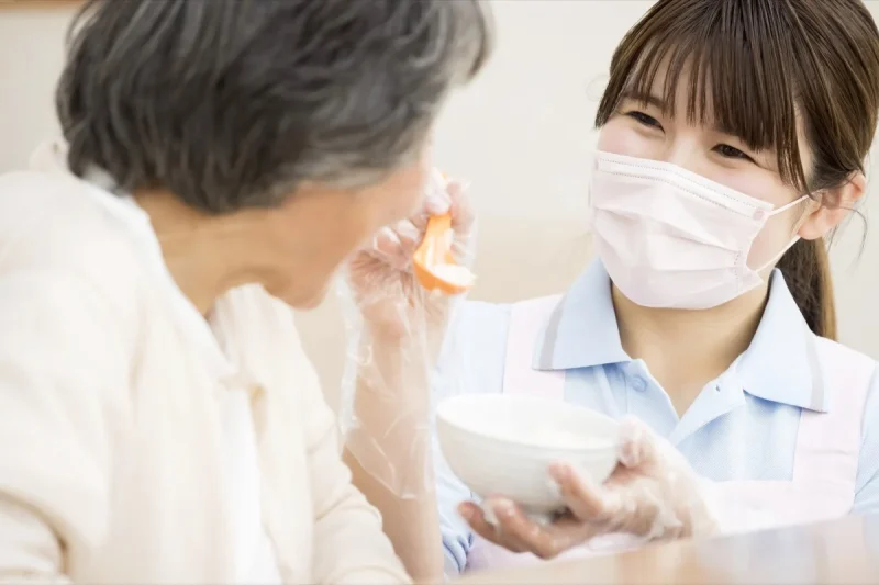 マスクを着けた女性職員が、高齢女性の水分補給を介助する場面